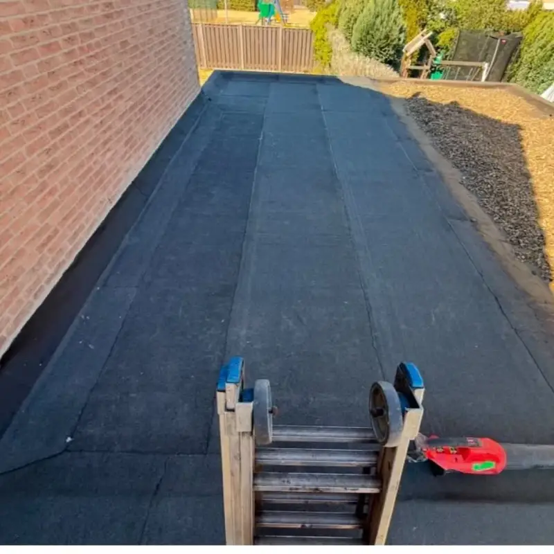 Nieuwe bitumen dakbedekking met een waterdicht afgewerkte aansluiting tussen gevel en garagedak met loodvervanger